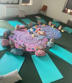 a studio laid out with yoga mats on the floor in a circle with parents and babies sitting or lying on them. On one mat is a baby massage demo doll.