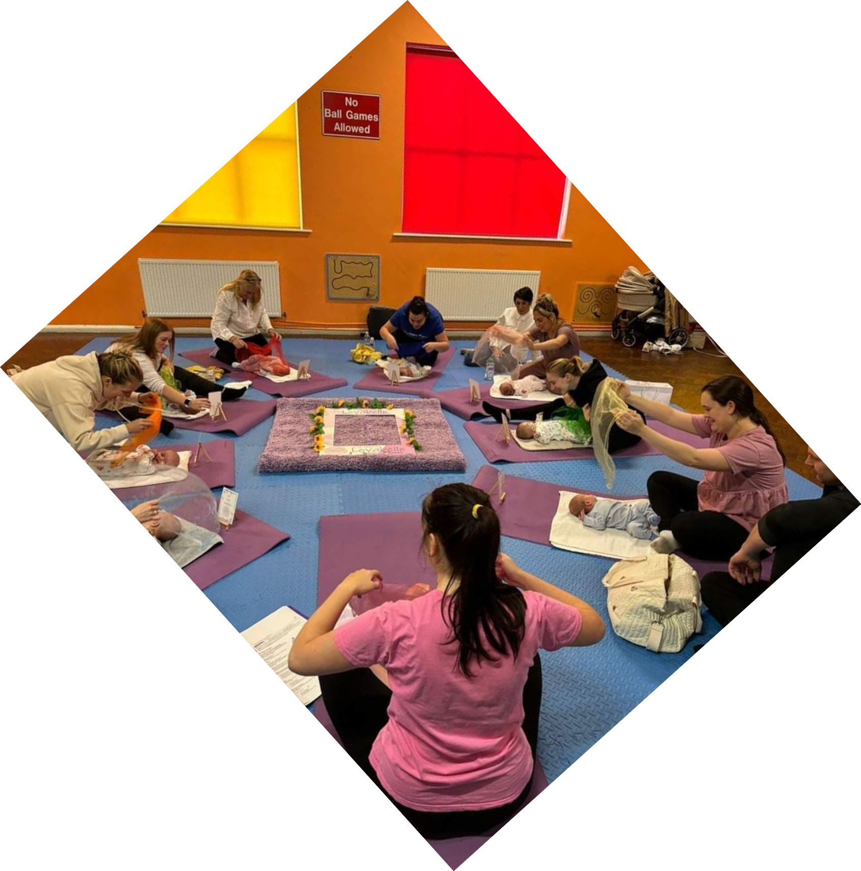 a photo of a group of women with babies on mats in front of them. The women are holding coloured scarves which they are wafting over their babies.