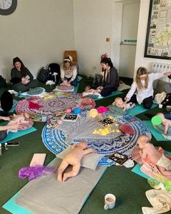 a photo of a rug with cream candles on it which has baskets around it with baby massage resources in them. In the foreground is a mortar board shaped sign saying "Today I graduated from Mummy and Baby Buddies Baby Massage